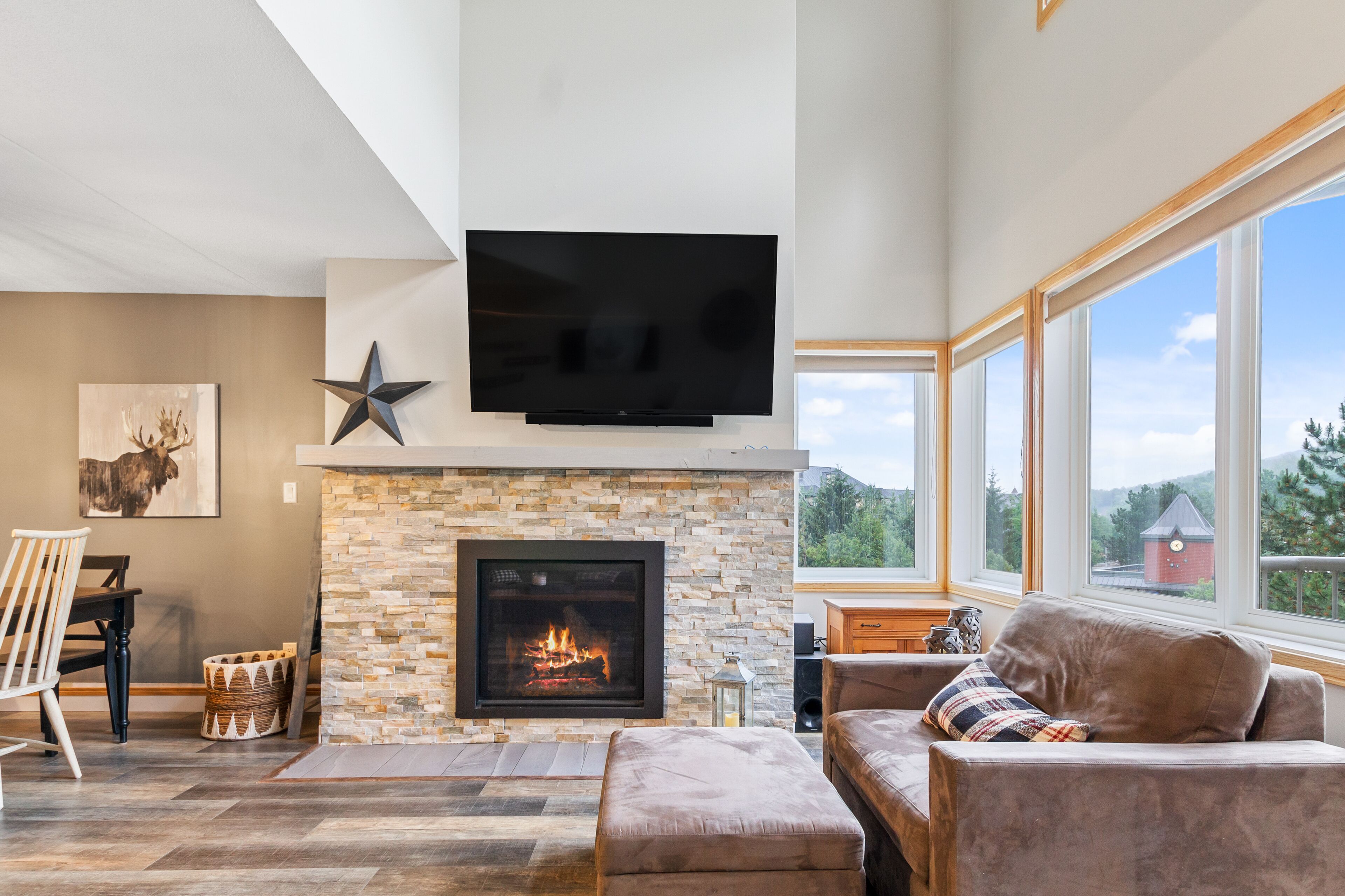A modern living room with a stone fireplace, a flat-screen TV, and a large window offering a view of the outdoors.