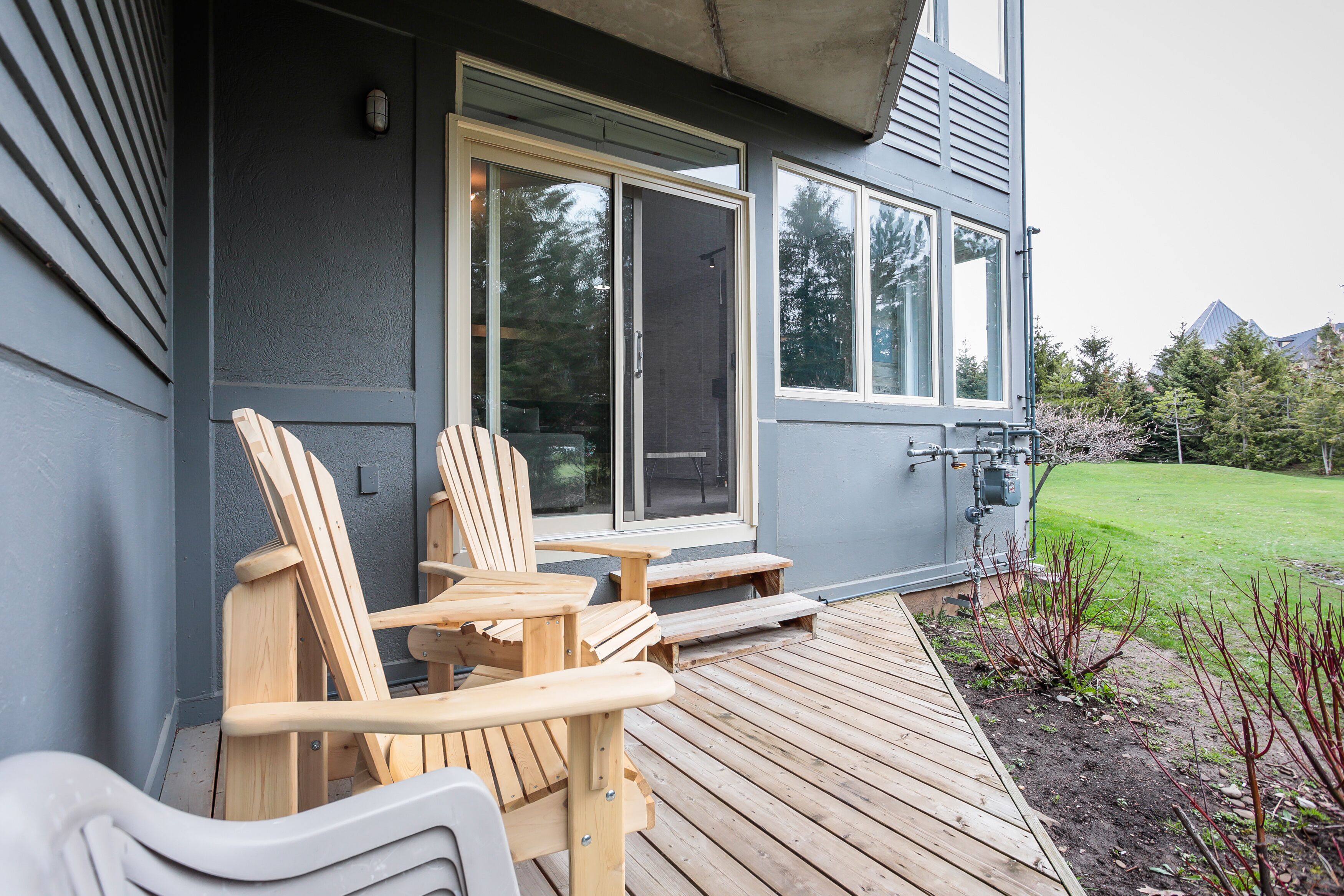 Una terraza de madera con dos sillas Adirondack, una mesita y una puerta corrediza que da a un patio.