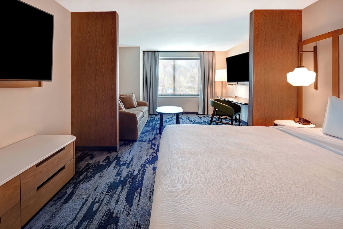 A hotel room with a large bed, a desk, a chair, a sofa, a TV, and a window with curtains.