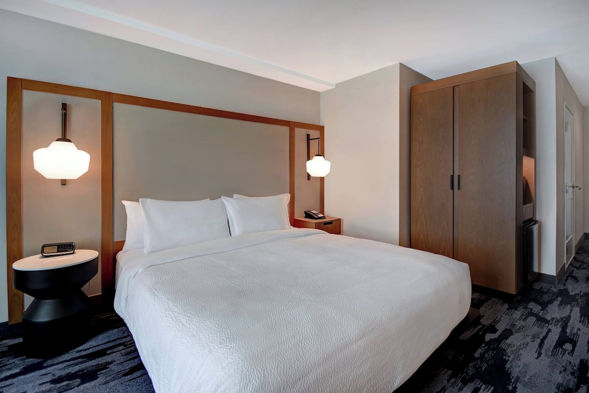 A hotel room with a large bed, two bedside tables with lamps, a wardrobe, and a carpeted floor.