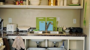 Een keuken met een dubbele spoelbak, een broodrooster en diverse keukengerei op planken.