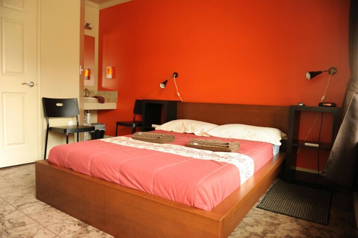 Un dormitorio con una cama de madera, una silla, un escritorio y una mesita de noche con lámparas.