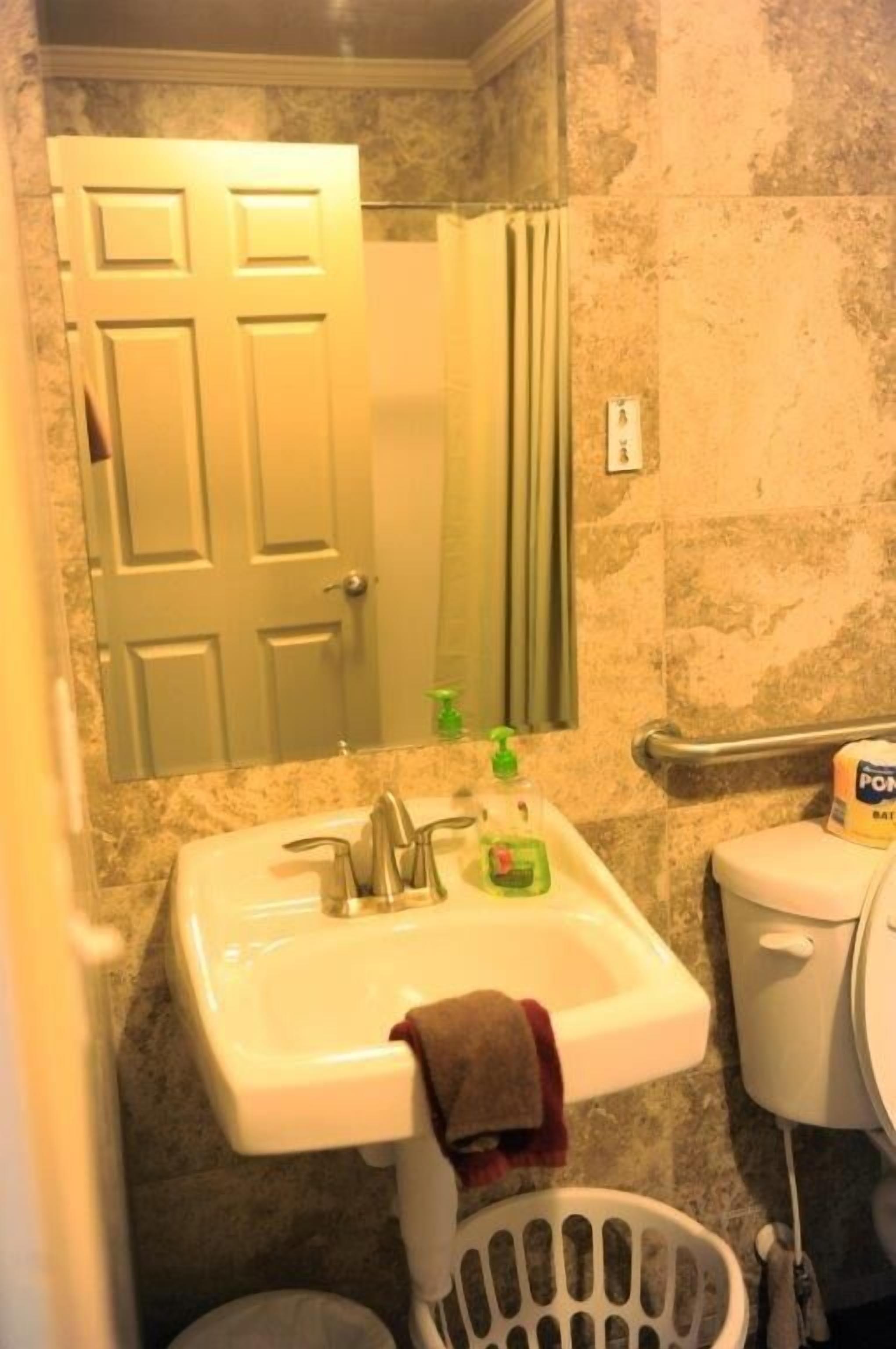 A bathroom with a white sink, a mirror, a towel hanging on the sink, a toilet, and a laundry basket.