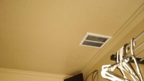 Een kamer met een witte deur, een zwart bureau met een witte ventilator, een zwarte speaker en een witte hanglamp.