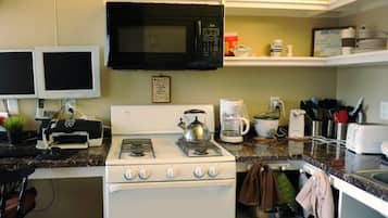 A kitchen with a stove, microwave, and coffee maker. There are two televisions mounted on the wall.