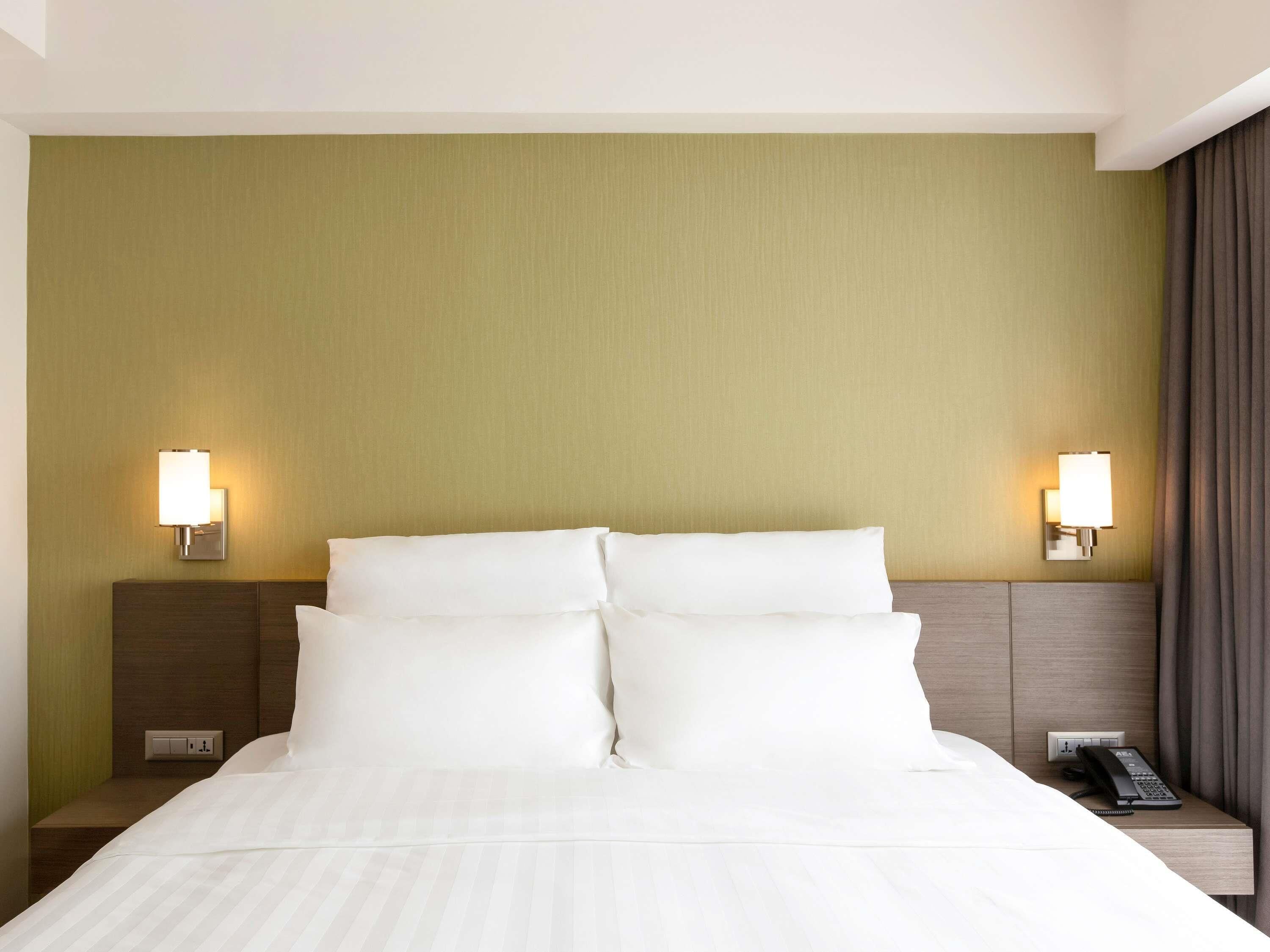 Ein Hotelzimmer mit einem Bett, zwei Nachttischlampen, einem Nachttisch mit Telefon und einer Steckdose.