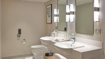 A modern bathroom with a toilet, two sinks, a large mirror, and a towel rack.