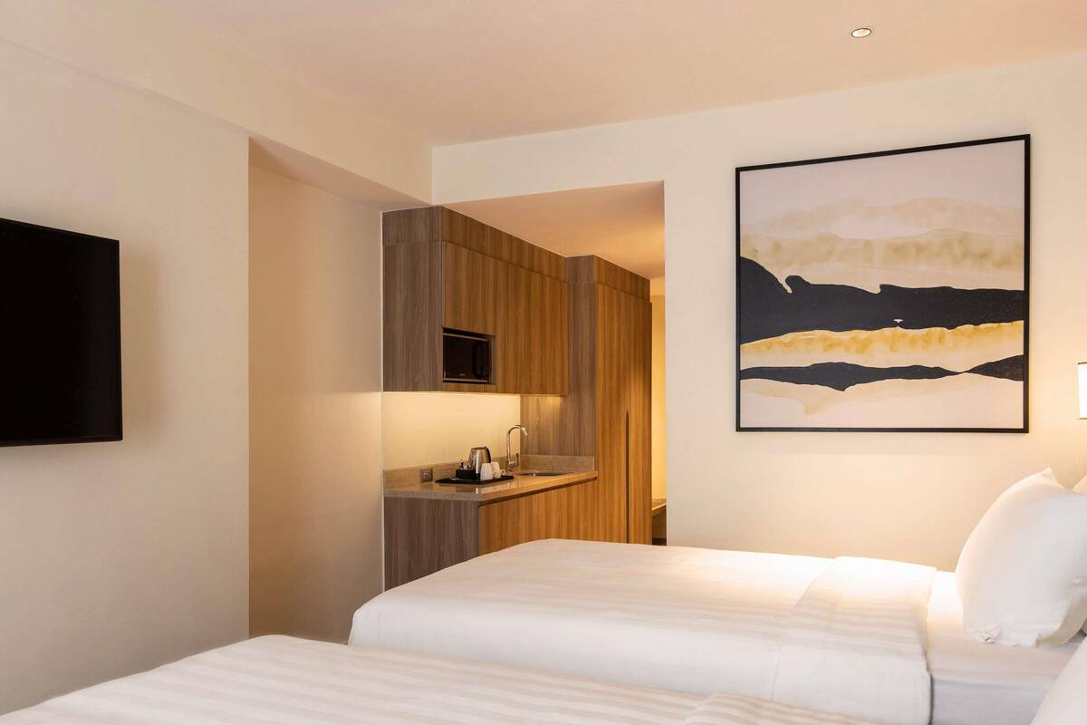 Une chambre d’hôtel avec deux lits, un téléviseur à écran plat fixé au mur, un four à micro-ondes et un tableau représentant un paysage.