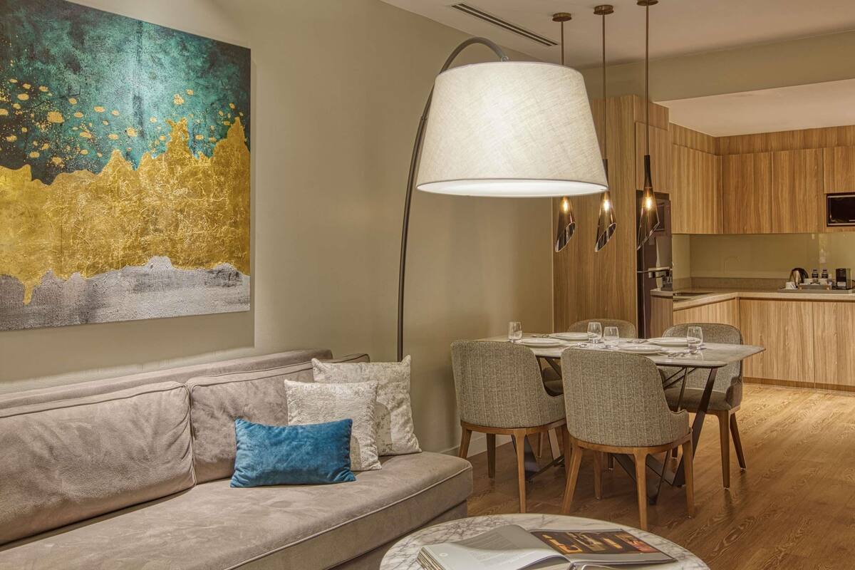 A modern living room with a sofa, a dining table with chairs, a large floor lamp, and a kitchen area.