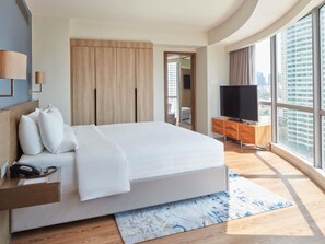 A modern hotel room with a large bed, a TV, a desk with a phone, and a view of the city. - Novotel Suites Manila at Acqua (Mandaluyong)