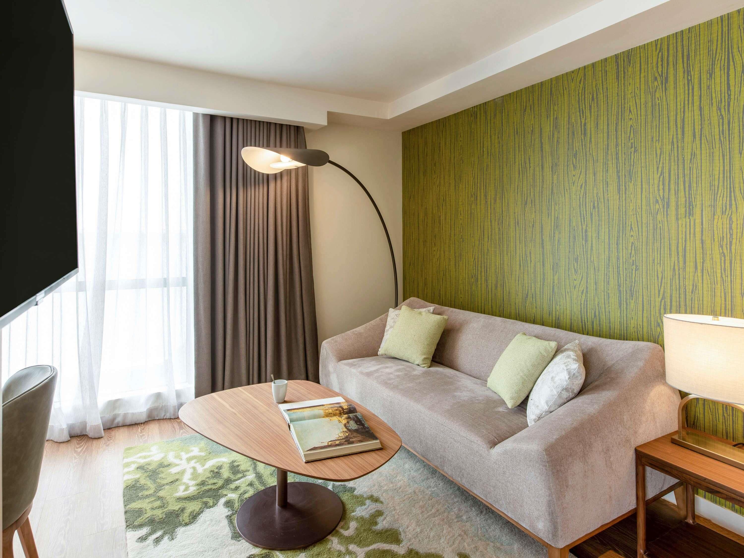 Une chambre d’hôtel moderne, équipée d’un canapé, d’une petite table, d’une lampe et d’un téléviseur.