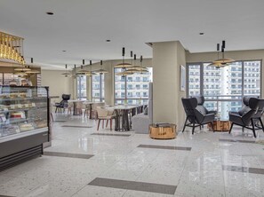 Eine moderne Hotellobby mit einer Bäckereiauslage, einer Sitzecke und großen Fenstern mit Blick auf die Stadt.