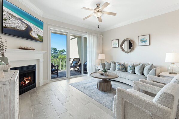 A living room with a fireplace, a ceiling fan, a large TV, a sofa, and a dining area with outdoor access. - Recently Updated 3 bedroom 3 bath Condo at Sanctuary at Redfish (Santa Rosa Beach)