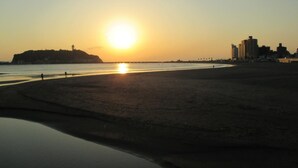 A beach with a sunset, calm water, and buildings in the background.