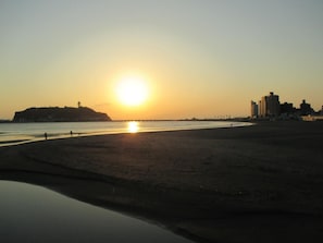 Una playa con atardecer, agua tranquila y edificios al fondo.