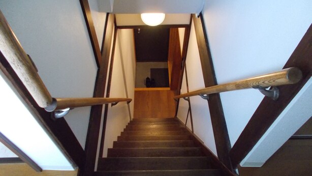 A wooden staircase with a handrail, leading to a room with a dark ceiling and a light fixture. - Akitaya Annex (Kamakura)
