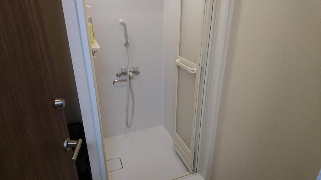 A small, enclosed shower area with a white door and a showerhead.
