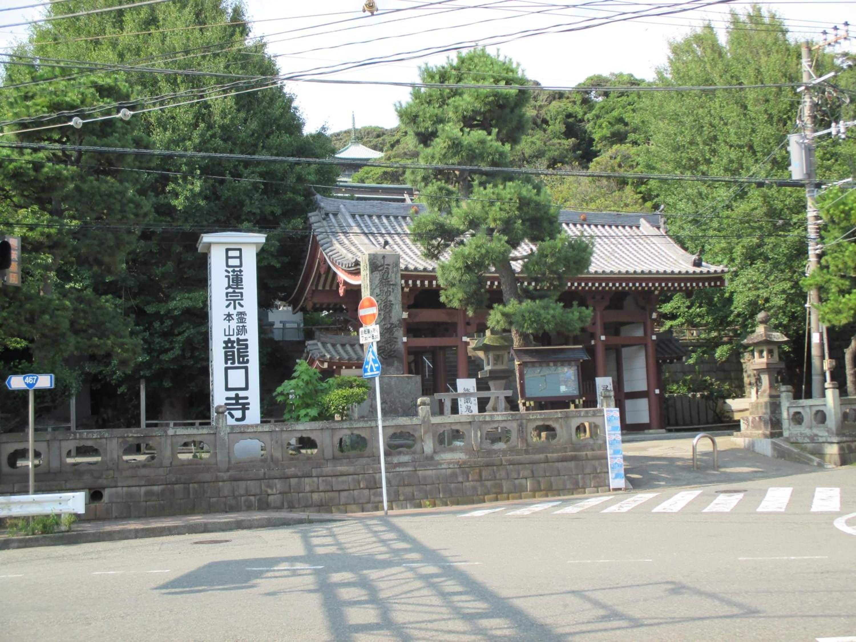 A traditional Japanese temple with a stone gate, a clear sky, and a street in the foreground.