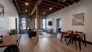 A spacious room with a wooden ceiling, a sofa, a dining table, and a TV mounted on the wall. - Executive Suite with King Bed and Fast Wi-Fi (Spokane)