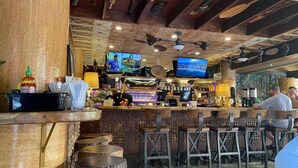 A rustic bar area with wooden stools, a counter with various items, and a television mounted on the wall.