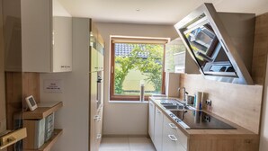 A compact kitchen with wooden cabinets, a built-in oven, a window with a view of a house, and a sink.