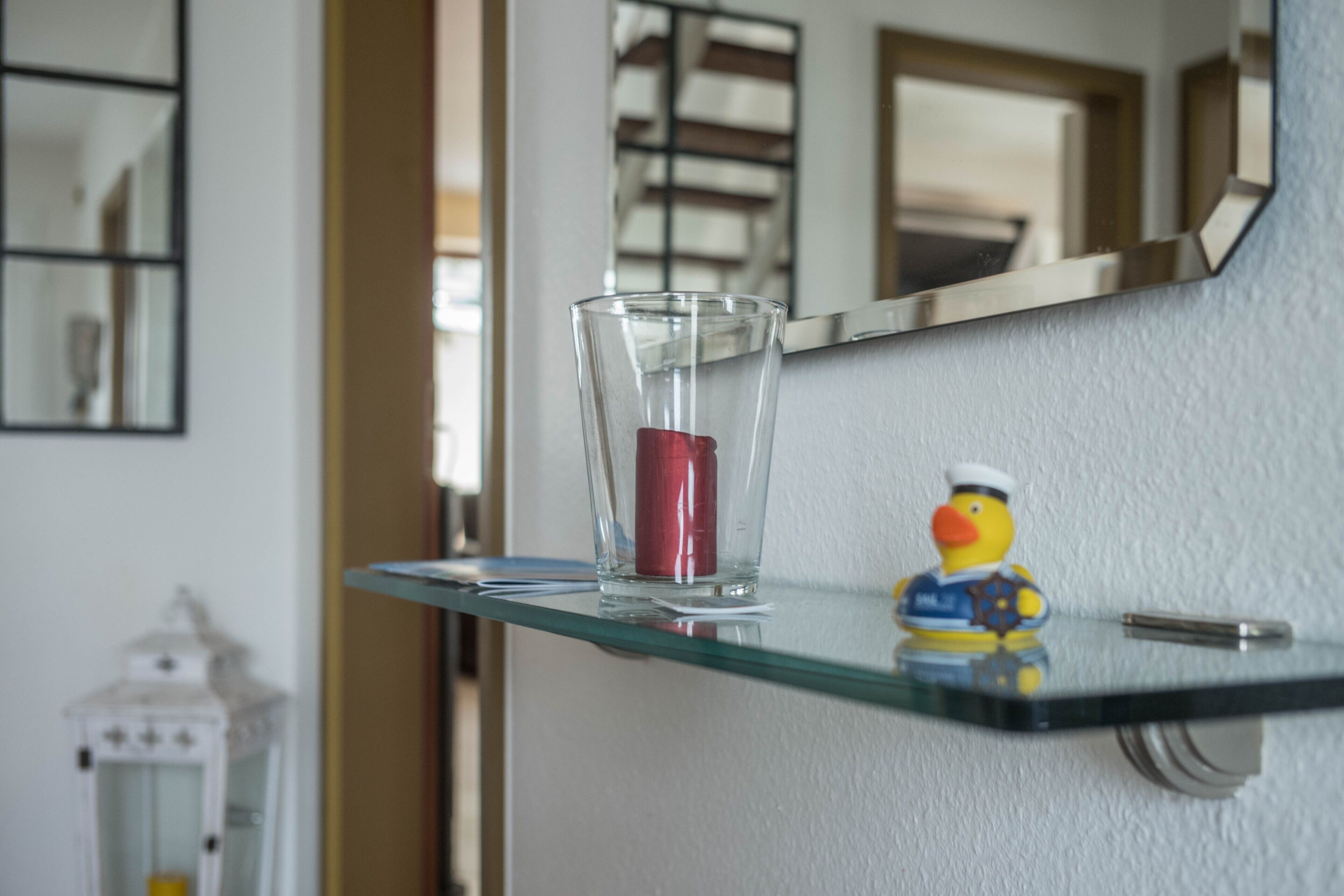 Un verre transparent posé sur une étagère en verre, avec un canard en caoutchouc et un stylo à côté.