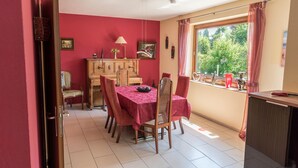 A dining area with a table set for four, a wooden cabinet, and a window with a view of greenery.