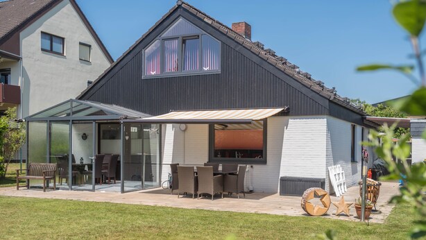A modern house with a glass-enclosed patio, outdoor furniture, and a clear view of the interior.