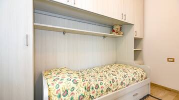 A single bed with a floral bedspread, a small shelf with a teddy bear, and a wardrobe with two doors.