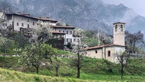 A rural setting with a building featuring a bell tower, surrounded by greenery and mountains. - Casa Doss Apartment with Lake View, Private Terrace, and Wi-Fi (TREMOSINE)