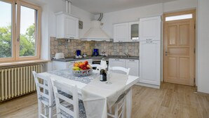 A kitchen with white cabinets, a tiled backsplash, a dining table with chairs, and a window with a view of trees. - Casa Doss Apartment with Lake View, Private Terrace, and Wi-Fi (TREMOSINE)
