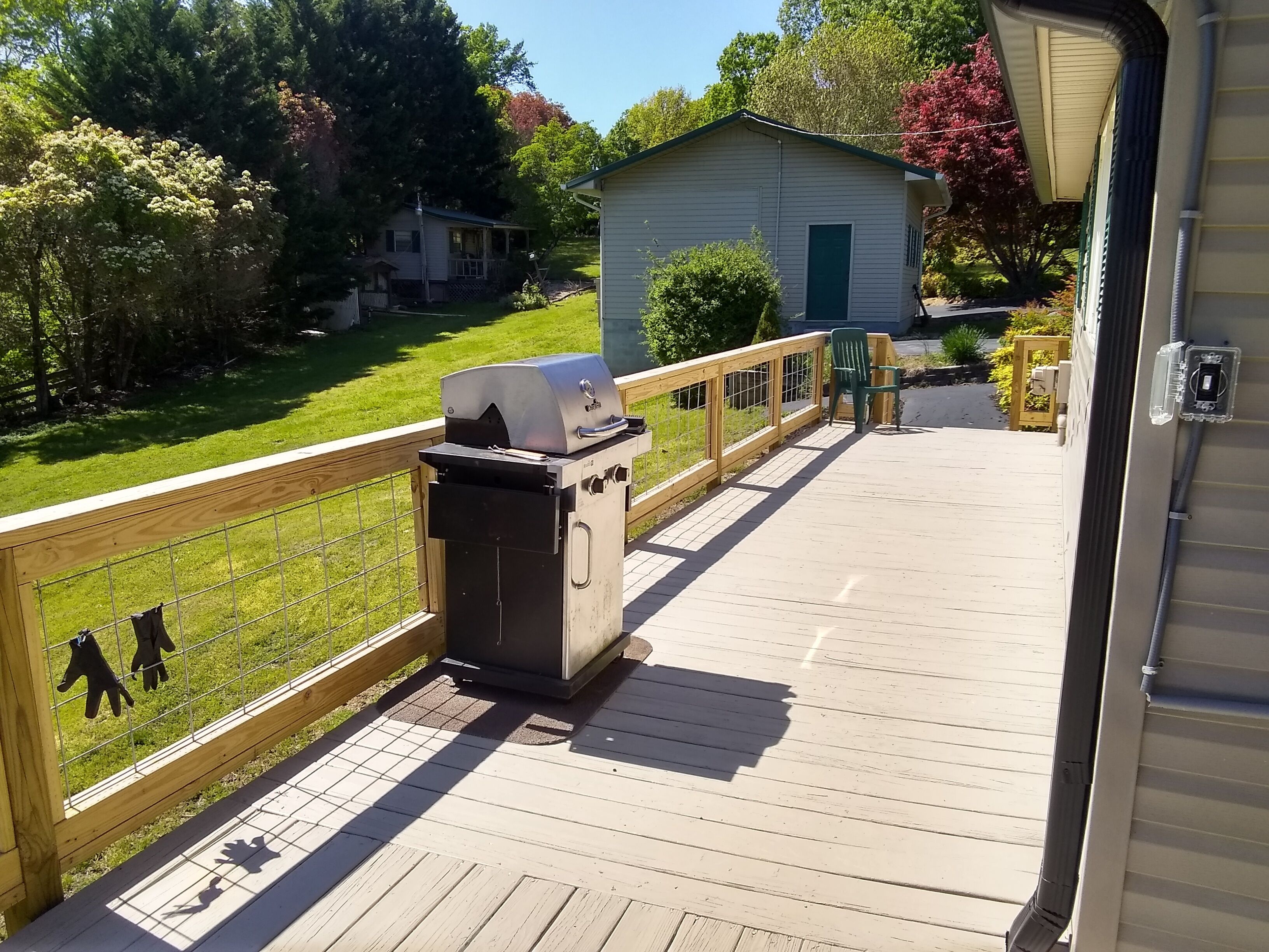 A wooden deck with a barbecue grill, a small shed, and a fenced area with two figures.