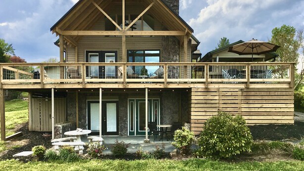 Une maison en bois à deux étages, dotée d’un balcon, d’un espace salon extérieur et d’une cheminée en pierre.