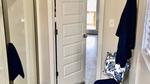 Un couloir avec un plancher en bois, une porte blanche et un banc sur lequel sont pliés des vêtements.