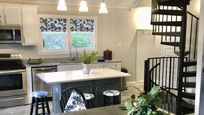 Une cuisine moderne dotée d’un îlot central, d’appareils électroménagers en acier inoxydable et d’un escalier en colimaçon noir.