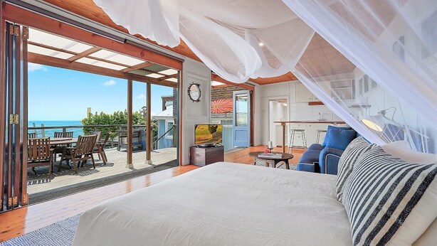 Une chambre avec un grand lit, un balcon avec une table et des chaises, et une vue sur l’océan.