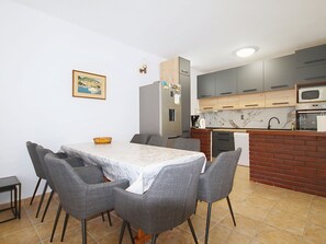 A modern kitchen with grey cabinets, a marble countertop, and a dining area with a table and chairs.