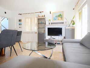 A living room with a sofa, a glass coffee table, a TV, and a dining area with a table and chairs.