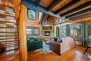 A log cabin interior with a fireplace, wooden floors, green sofas, and a stone wall. - Modern Log Cabin - Two Masters, Hot tub, Wi-Fi, Views, Fishing, and Easy Roads! (Sevierville)