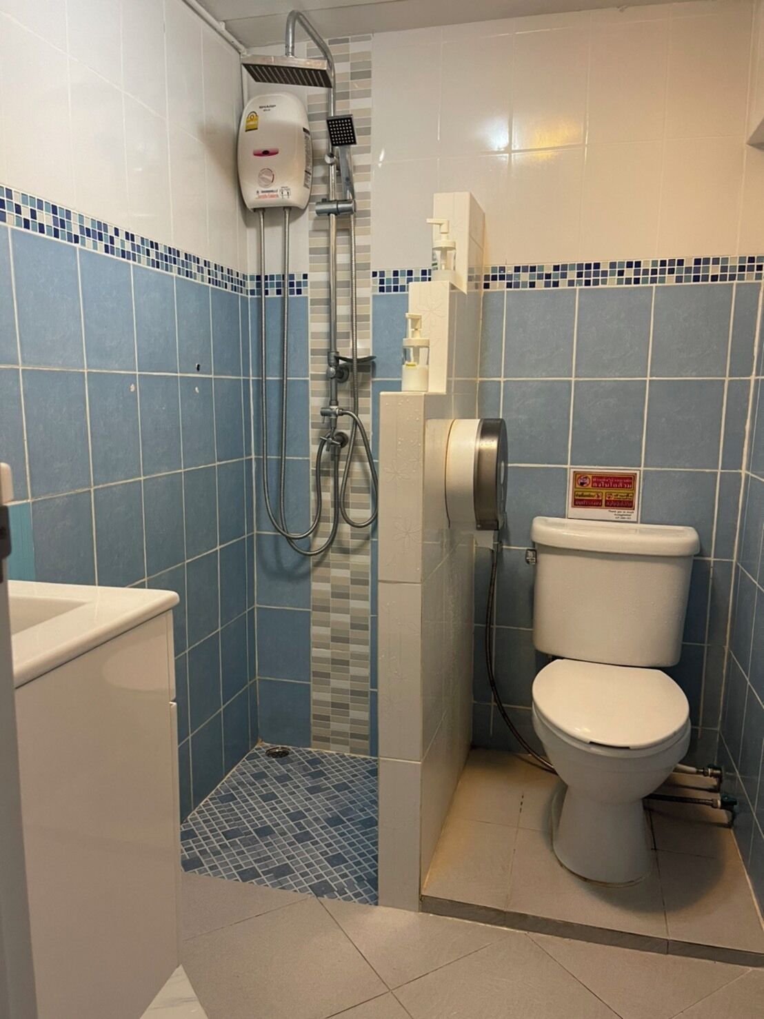 Un baño pequeño con azulejos blancos y azules, un inodoro blanco y una cabina de ducha.