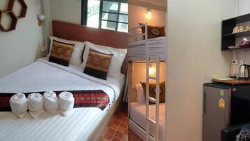 A room with a bed, a bunk bed, a small refrigerator, a table, and a wall-mounted shelf.