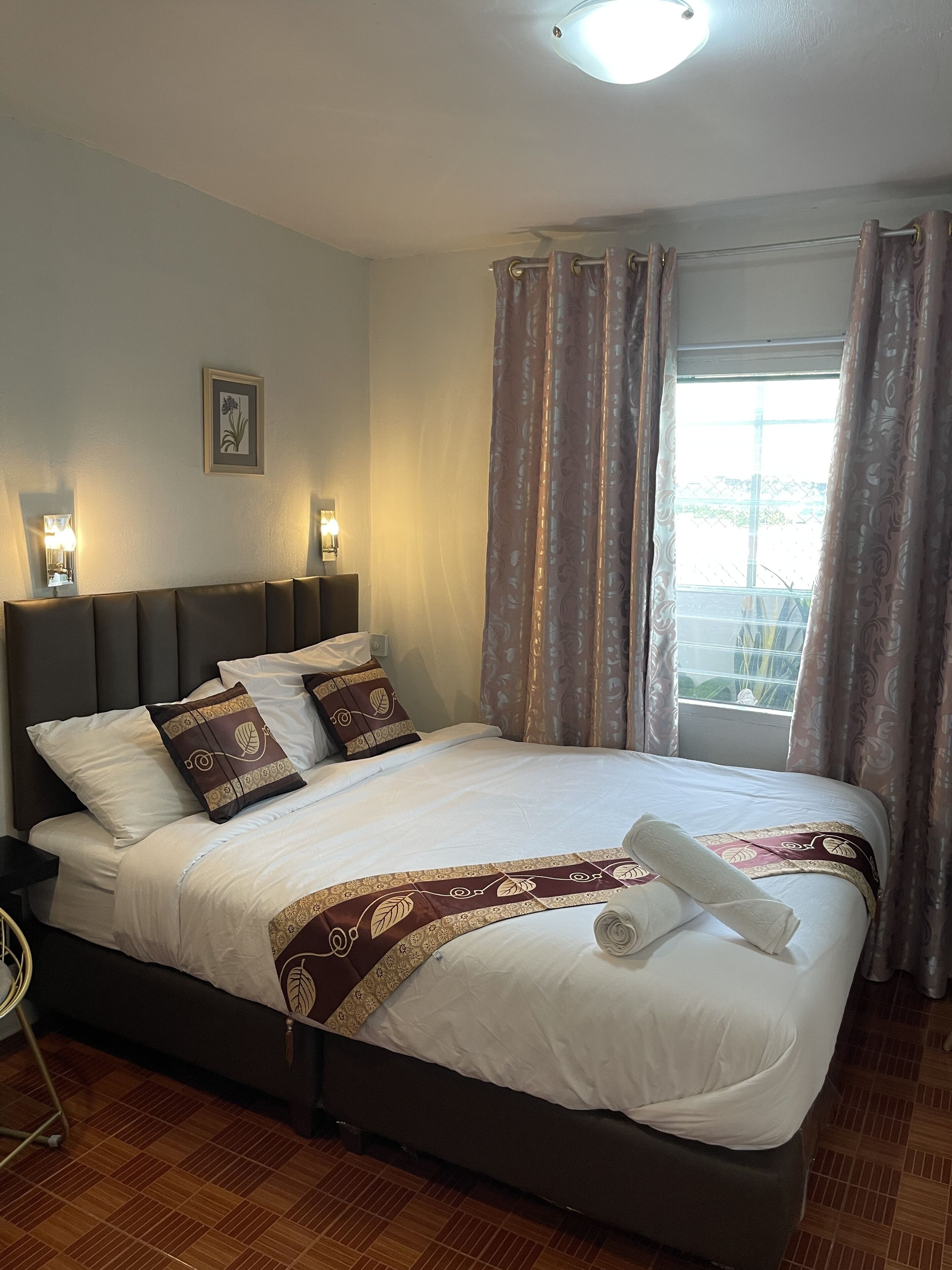 Un lit bien fait, avec une couvre-lit à motifs, une tête de lit et une table de chevet sur laquelle se trouve une lampe.