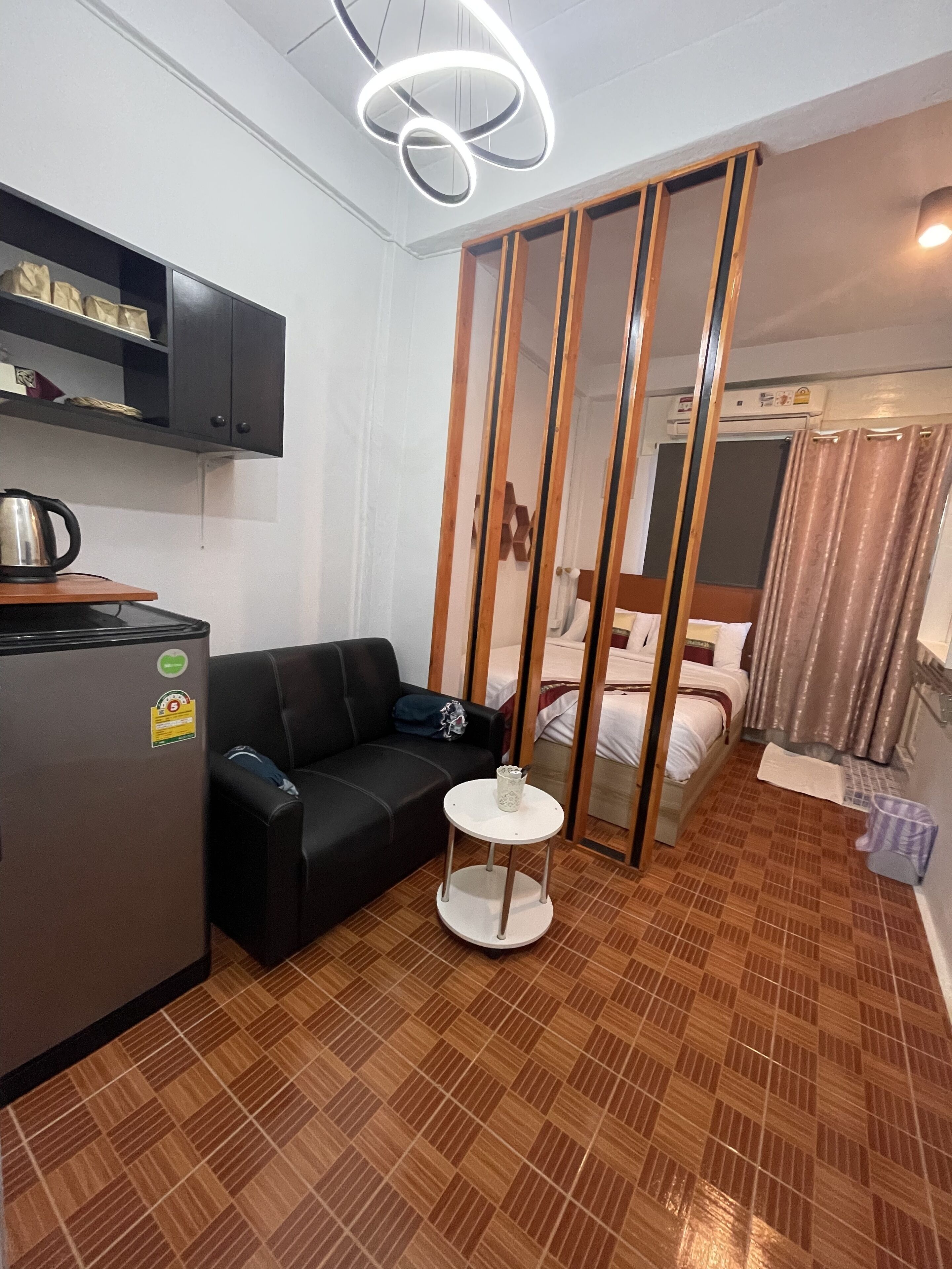 Une chambre d’hôtel compacte comprenant un coin cuisine, un canapé noir, une petite table ronde et un lit doté de rideaux.