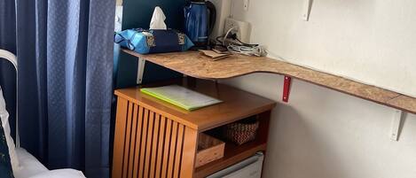 A hotel room with a bed, a small desk with a kettle, a cabinet, and a trash bin.
