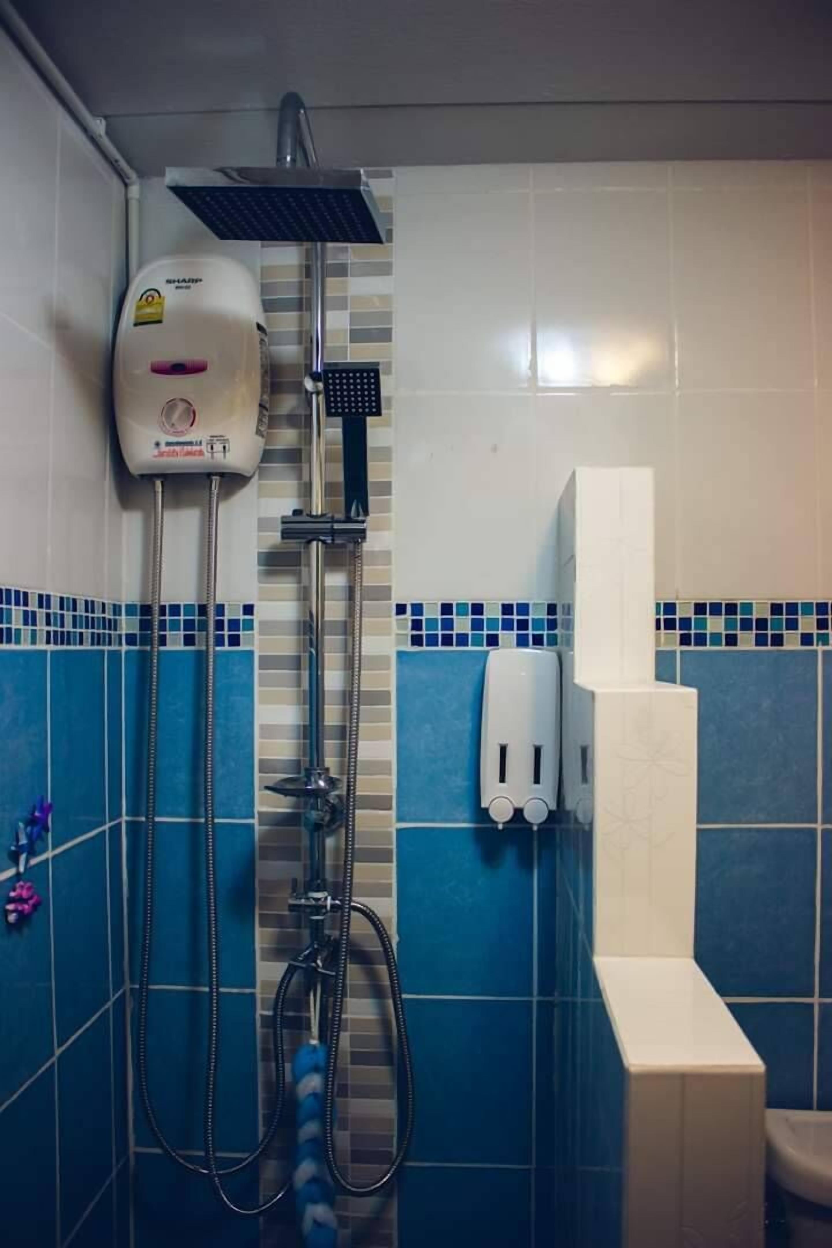 Un baño con ducha, dispensador de jabón y retrete.