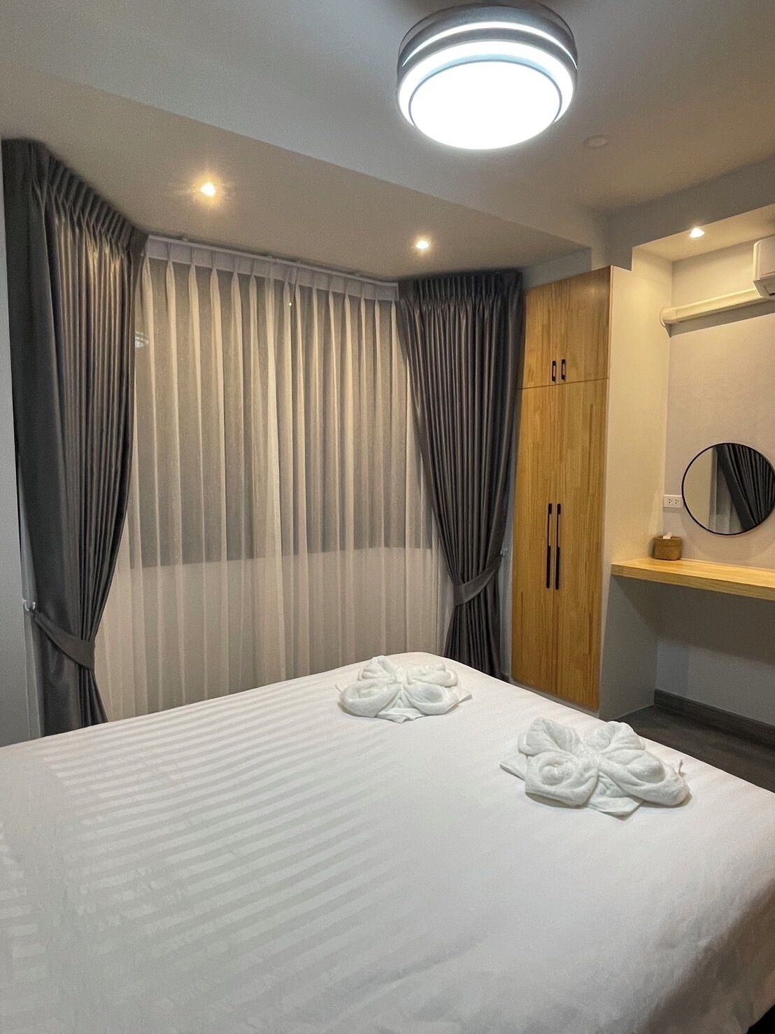 Ein Hotelzimmer mit einem Bett, Vorhängen, einem Holzschrank, einem Spiegel und einer Deckenleuchte.