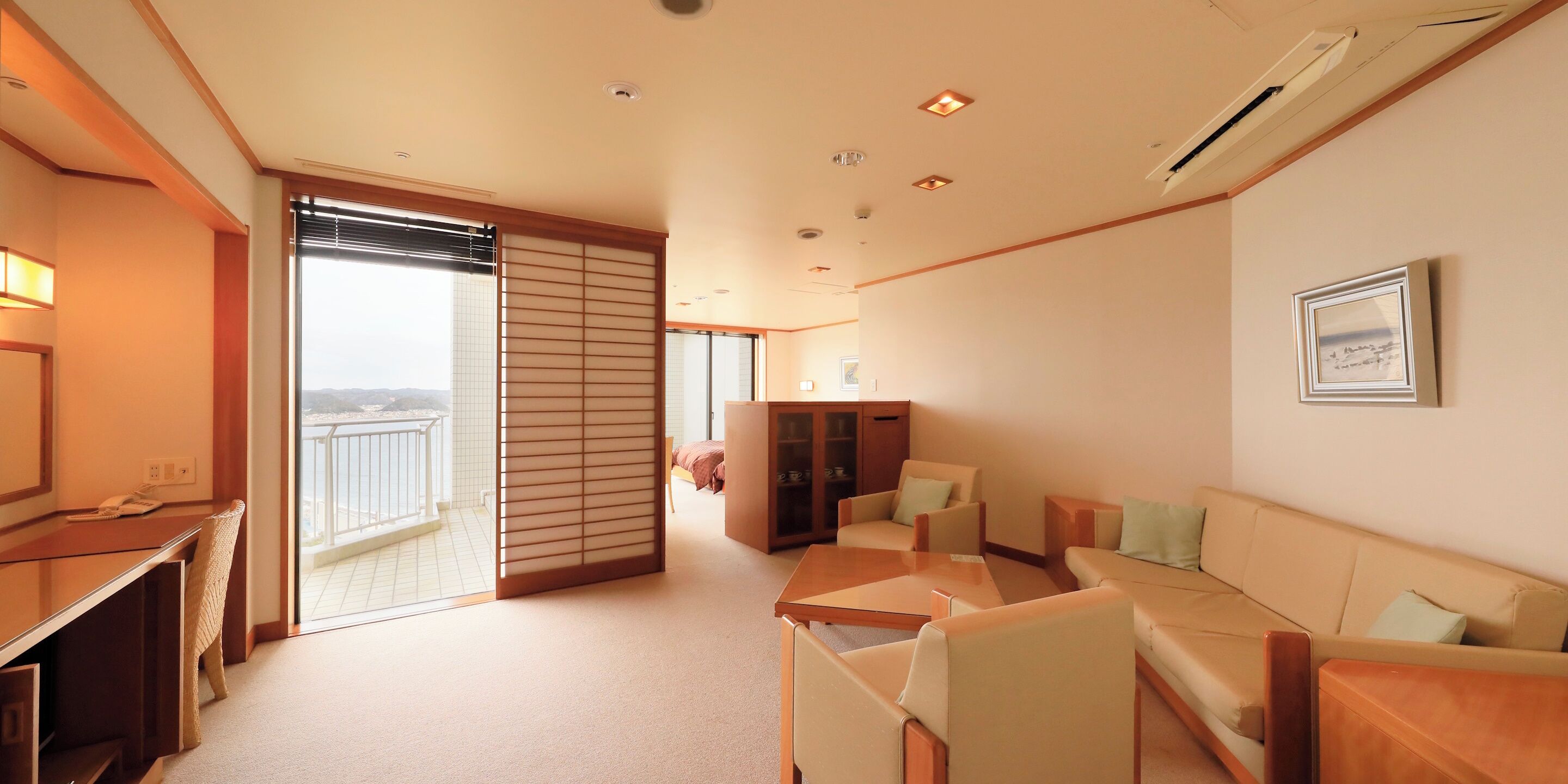 Habitación de hotel con balcón, sofá, escritorio y armario.