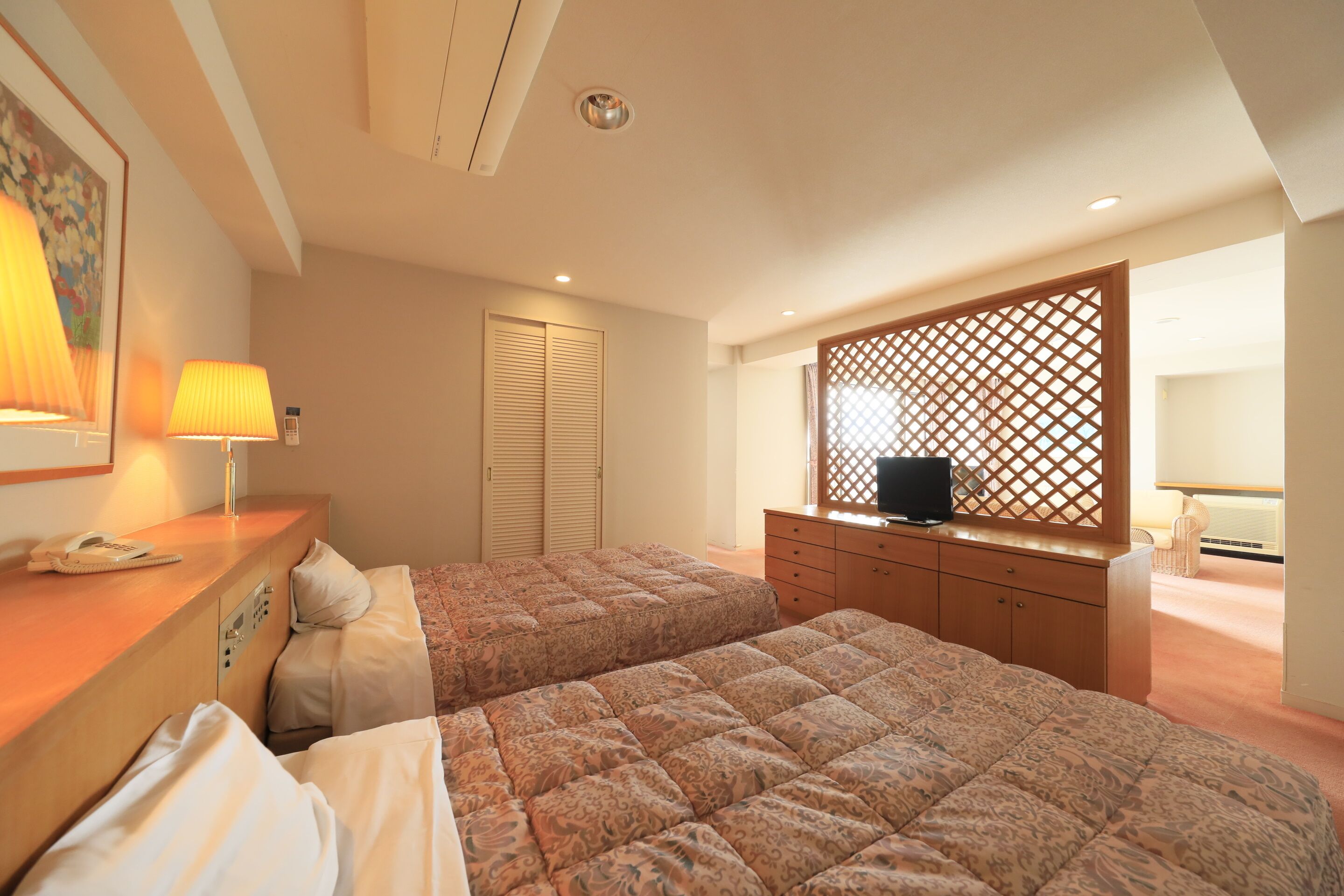 A hotel room with two beds, a wooden dresser, a TV on a wooden stand, and a decorative screen.