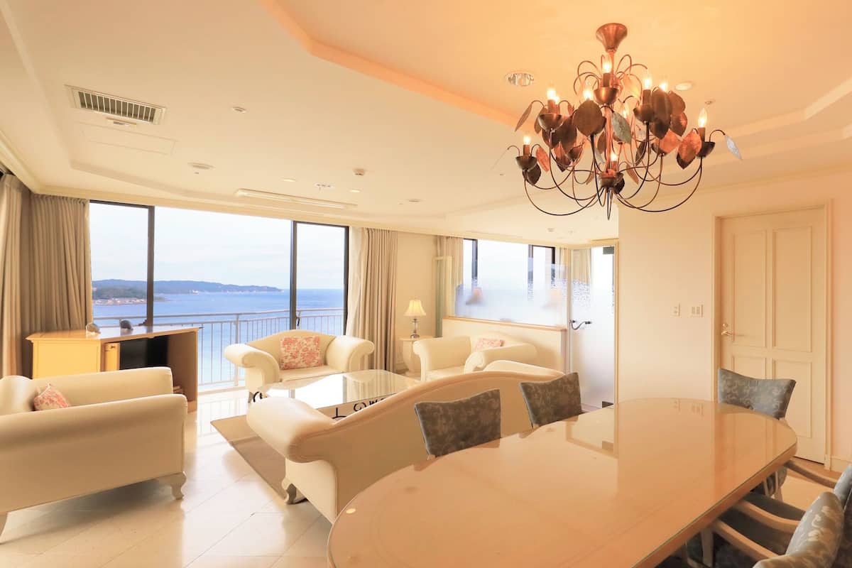 Une pièce spacieuse avec une grande table ronde, des sièges confortables, un lustre et une vue sur la mer.