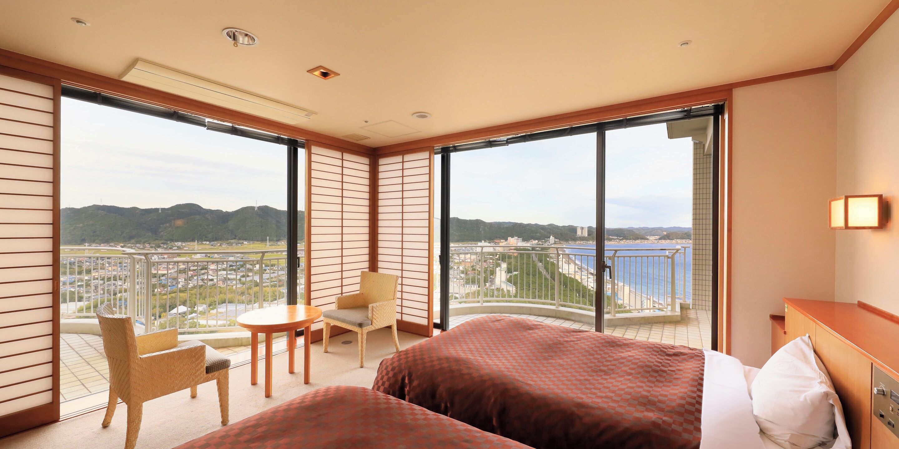 Habitación de hotel con balcón, cama, silla, mesa y vistas a la ciudad y al agua.